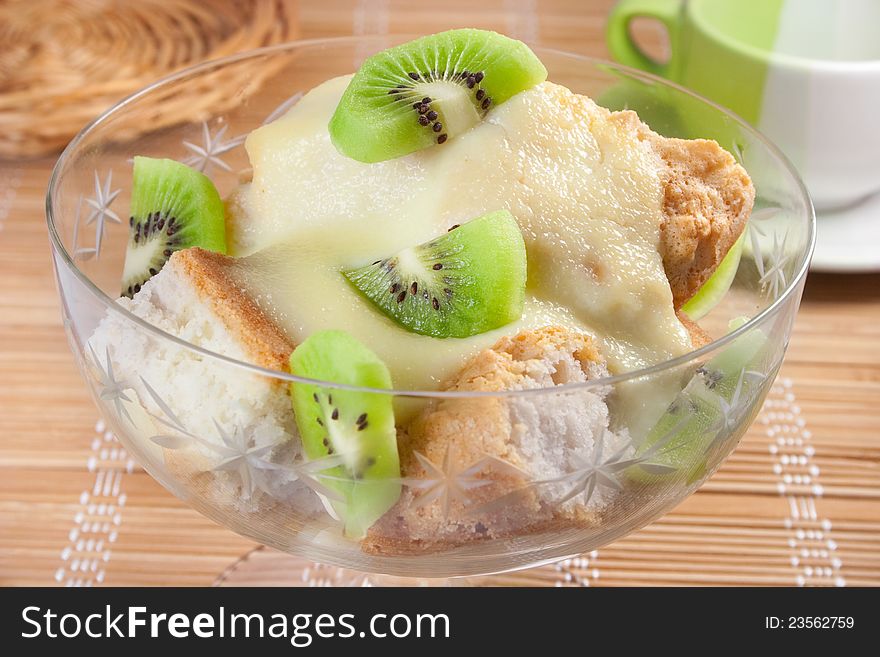 Dessert with slices of sponge cake, sweet cheese sauce and  kiwi in glass bowl on table. Dessert with slices of sponge cake, sweet cheese sauce and  kiwi in glass bowl on table