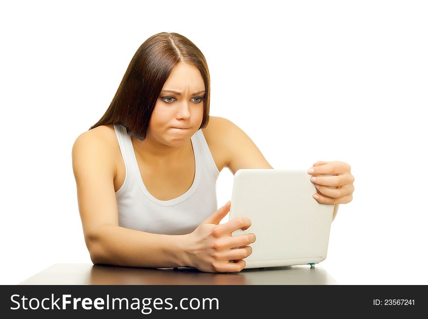 The young woman is upset and surprised with the laptop behind a table on a white background. The young woman is upset and surprised with the laptop behind a table on a white background