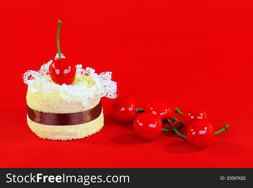 Rolled up towel with toy cherries on red background. Rolled up towel with toy cherries on red background