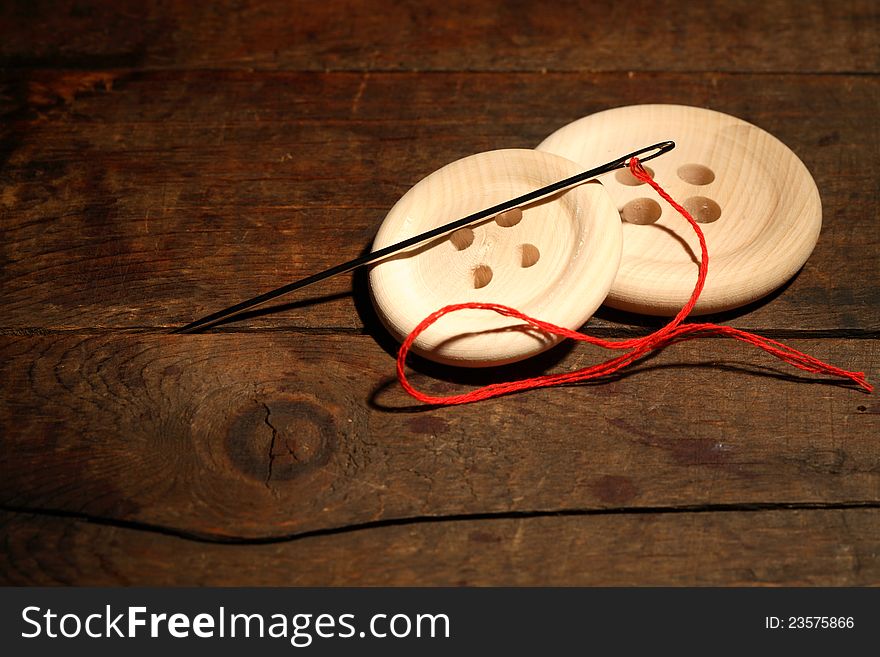 Sewing concept.Closeup of two wooden buttons and needle with thread on dark background. Sewing concept.Closeup of two wooden buttons and needle with thread on dark background