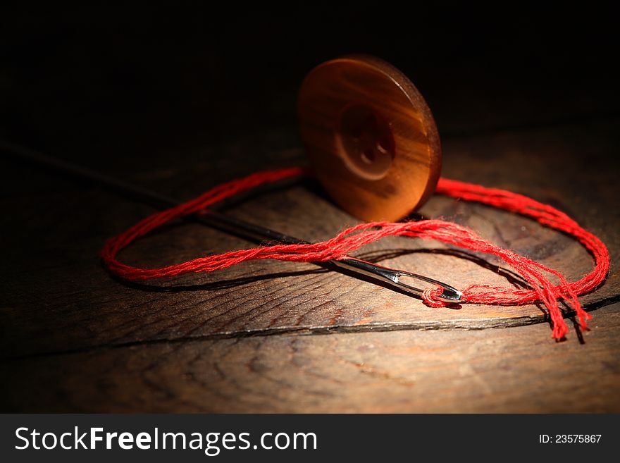 Sewing concept.Closeup of button and needle with thread on dark wooden background. Sewing concept.Closeup of button and needle with thread on dark wooden background