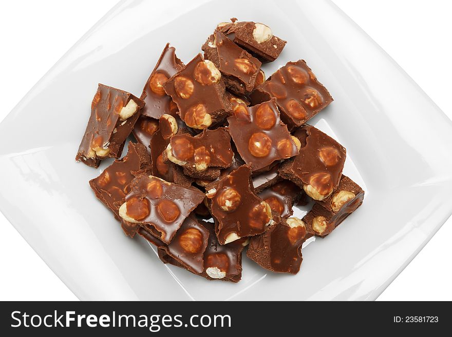 Broken chocolate pieces with nuts on white plate, top view, isolated. Broken chocolate pieces with nuts on white plate, top view, isolated