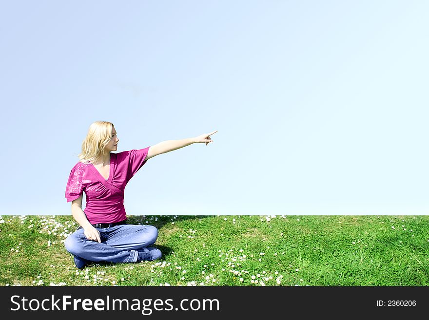 A young woman is sitting on a green meadow and show something. A young woman is sitting on a green meadow and show something