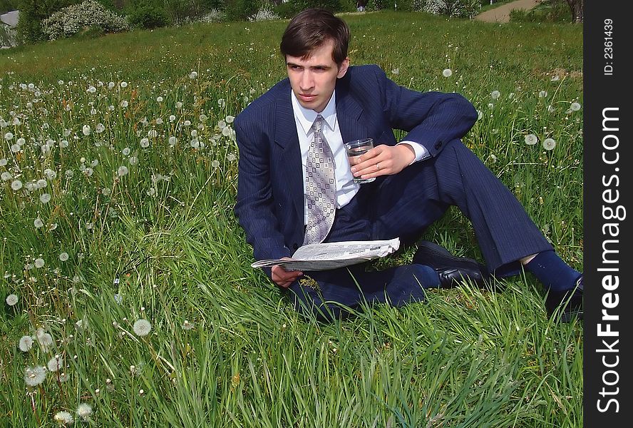 Young businessman sits on a lawn and holds newspaper. Young businessman sits on a lawn and holds newspaper
