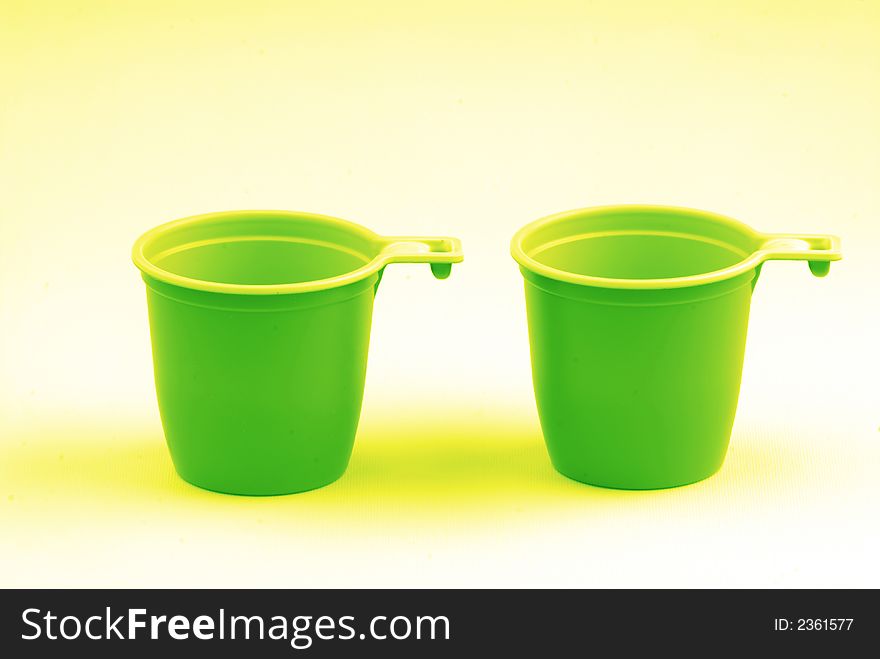 Two plastic glasses located on  white surface covered by green light