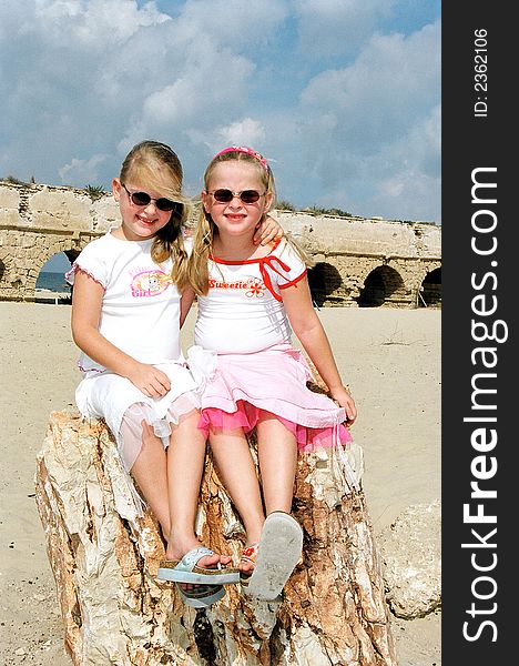 Girls twins sit on a stone in dark glasses. Girls twins sit on a stone in dark glasses