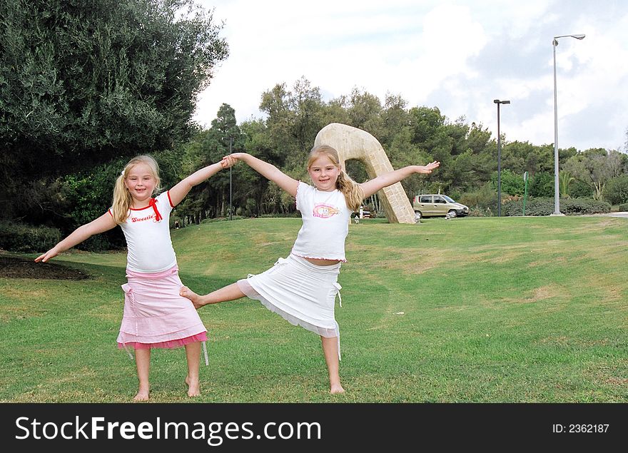 Girls twins on a grassy lawn are engaged in gymnastics. Girls twins on a grassy lawn are engaged in gymnastics