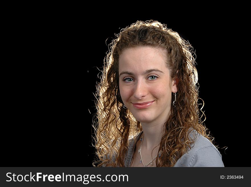 Teen girl portrait with curly hair smiling against a black background