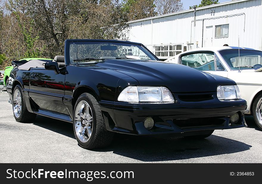1993 Ford Mustang convertible. Black car with clear headlamps, cowl hood and chrome wheels.