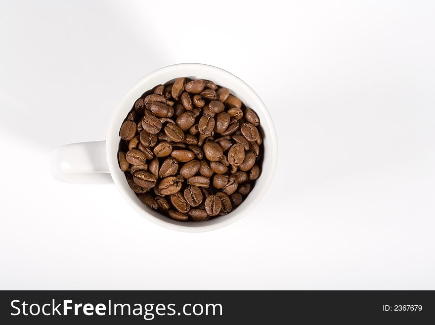 White mug, filled with good smelling coffeebeans on white background. View from above. White mug, filled with good smelling coffeebeans on white background. View from above.