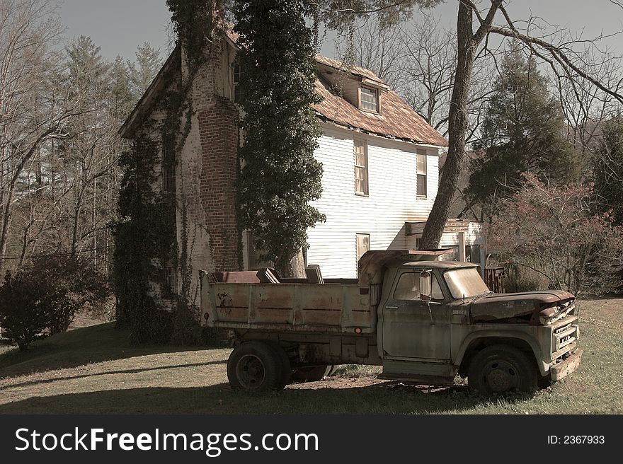 Antique dump truck in front of abandoned house, sepia tone