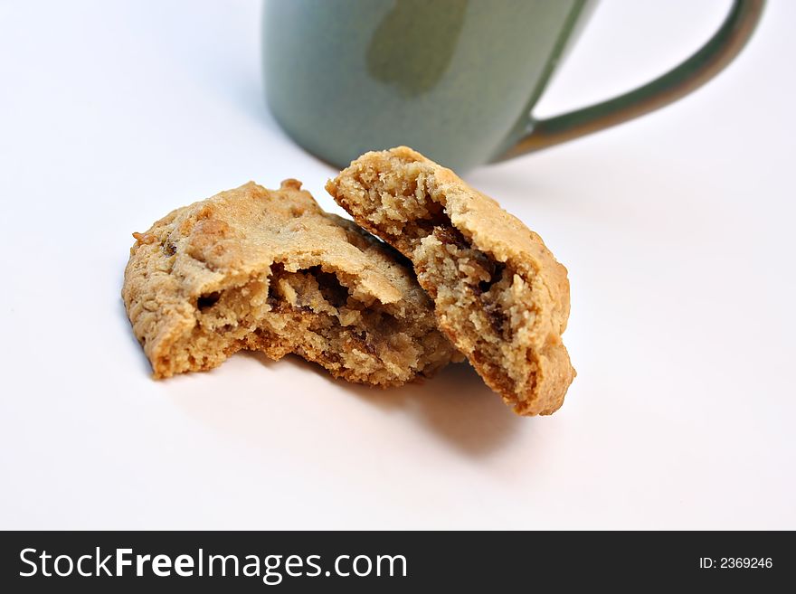 A cookie broken in half with a green coffee cup in the background isolated on white. A cookie broken in half with a green coffee cup in the background isolated on white