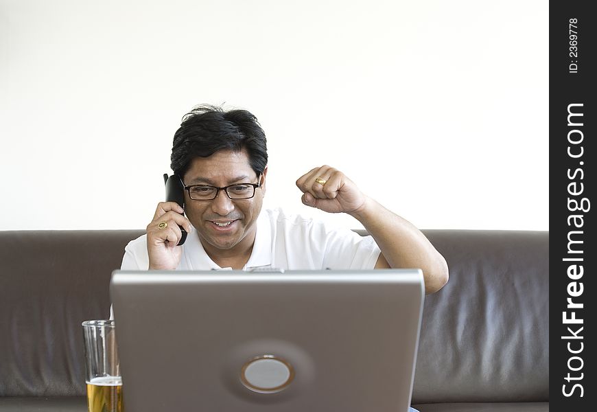 Asian man on leather couch drinking beer working on laptop happy relaxed relaxing winner. Asian man on leather couch drinking beer working on laptop happy relaxed relaxing winner