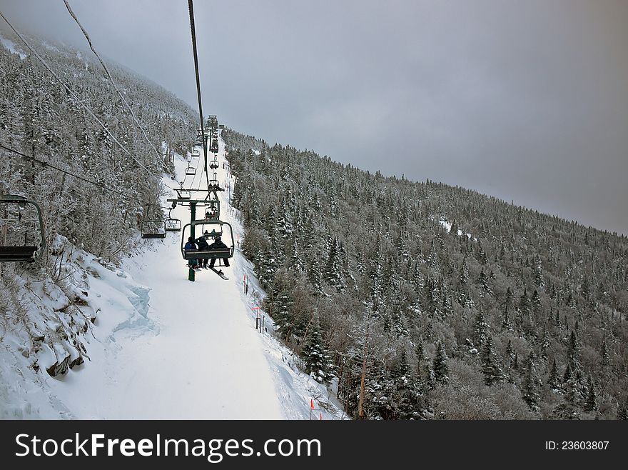 Ski lift ride takes skiers to the top of a snowy mountain among evergreen trees. Ski lift ride takes skiers to the top of a snowy mountain among evergreen trees.