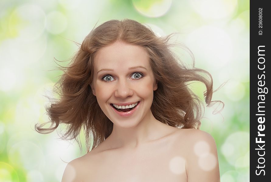 Beautiful cheerful girl with flowing hair laughs on the green background of the spring and summer outdoors. Beautiful cheerful girl with flowing hair laughs on the green background of the spring and summer outdoors