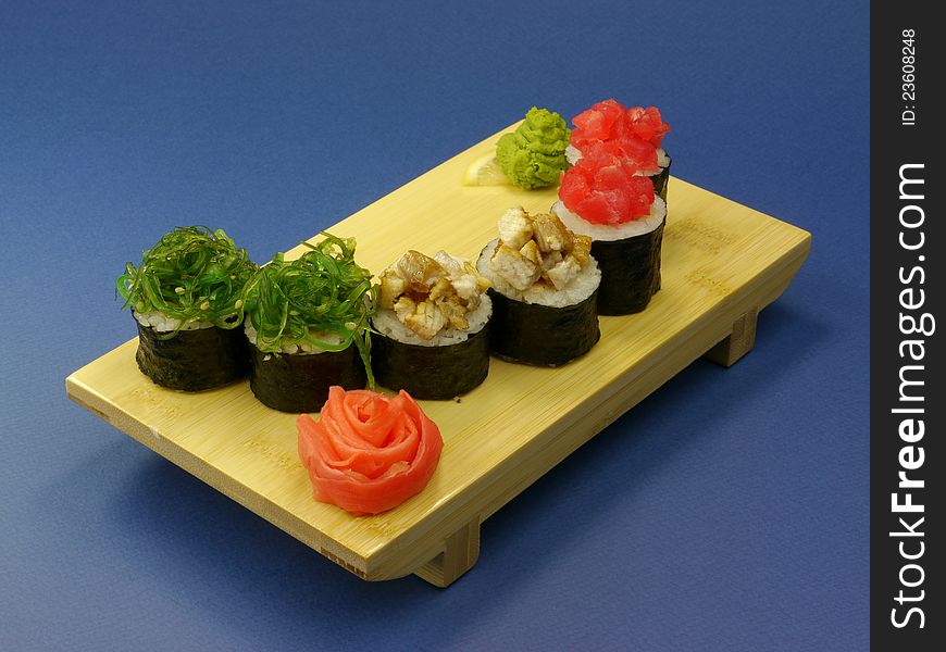 Delicious sushi rolls on wooden plate with pickled ginger and wasabi on blue background.