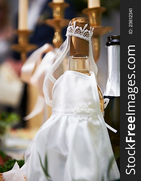 Bottle of champagne in costumes of bride on wedding table