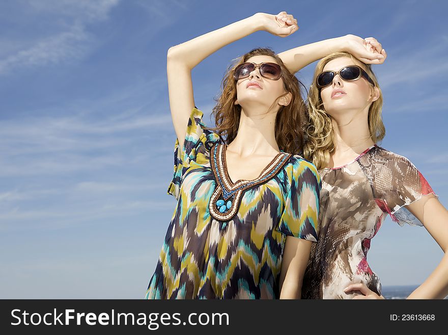 Two beautiful brunette and blonde girl in sunglasses on background blue sky. Two beautiful brunette and blonde girl in sunglasses on background blue sky