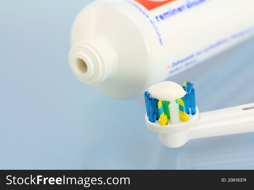 Toothpaste and a new electronic toothbrush head on a shiny blue background