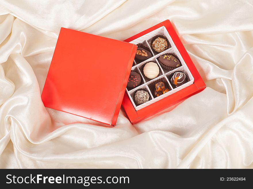 Red box of sweet handmade chocolates on white satin background. Red box of sweet handmade chocolates on white satin background