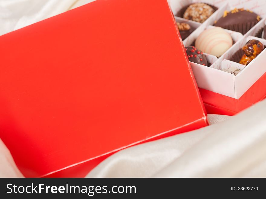 Red box of sweet handmade chocolates on white satin background. Red box of sweet handmade chocolates on white satin background