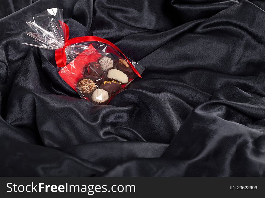 Transparent bag with chocolates and red ribbon on black satin background. Transparent bag with chocolates and red ribbon on black satin background