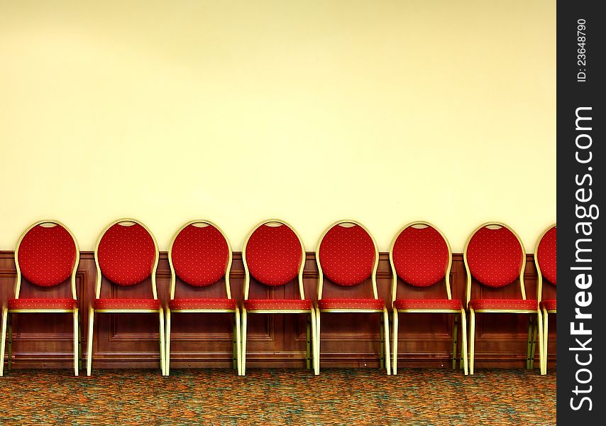 Red chairs lined up in a series  by yellow wall