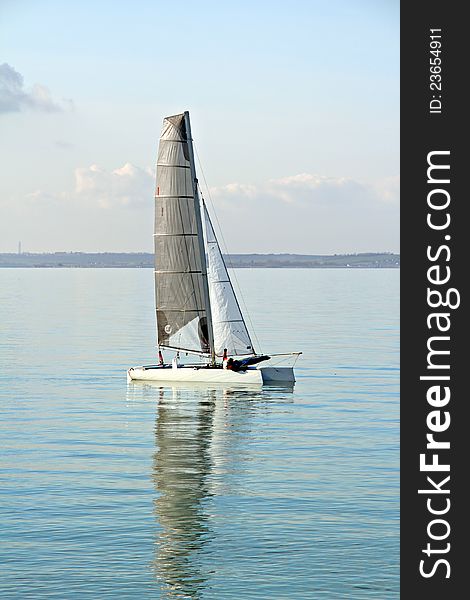 Photo of catamaran sailing just off the mainland showing nice reflection of sails in the water. Photo of catamaran sailing just off the mainland showing nice reflection of sails in the water.