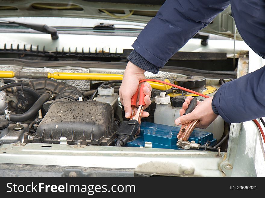 A mechanic using jumper cables to start a car battery.