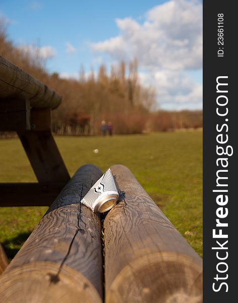 Discarded drinks can on a picnic bench at a parkland beauty spot. Two people walking away in the distance. Blue sky on a sunny day. Discarded drinks can on a picnic bench at a parkland beauty spot. Two people walking away in the distance. Blue sky on a sunny day.