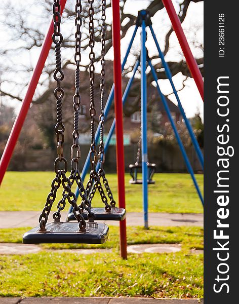 Row of childs swings in a playground setting.  Bright red and blue frames.  Nearest swings in sharp focus fading to toddler swings in distance. Row of childs swings in a playground setting.  Bright red and blue frames.  Nearest swings in sharp focus fading to toddler swings in distance.