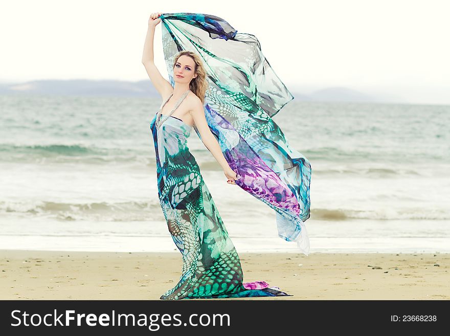 A beautiful woman on the beach with vibrant, colored fabric blowing in the wind.