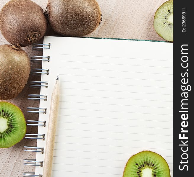 Directly above close-up view of a table with a kiwi and a notebook on cutting board. Directly above close-up view of a table with a kiwi and a notebook on cutting board