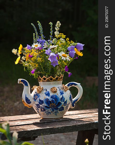 In the big teapot, painted with dark blue colours, a bouquet of wild flowers. In the big teapot, painted with dark blue colours, a bouquet of wild flowers