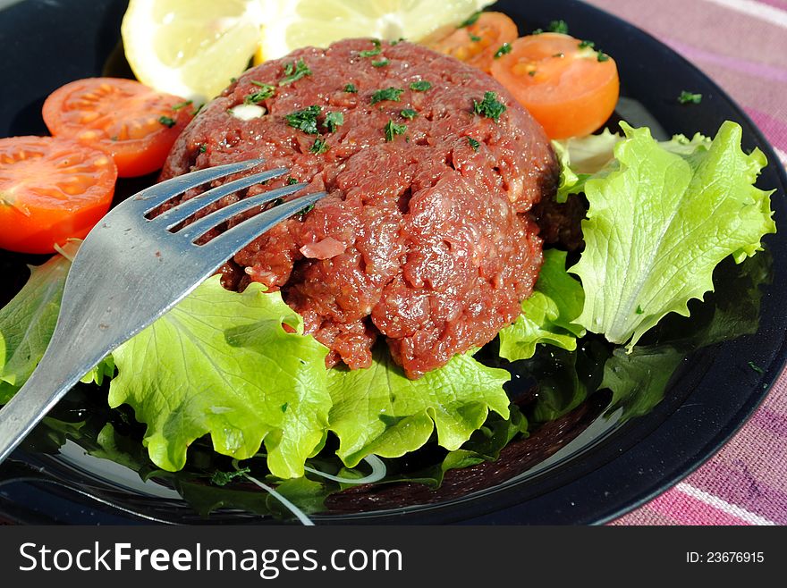 Raw ground beef with vegetables on a black dish