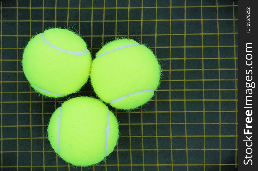 Three tennis balls on a racket strings