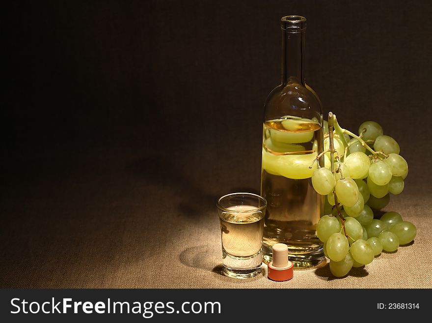 Glass full of grape Italian vodka ï¿½grappaï¿½ near bottle and bunch of grapes on old canvas background