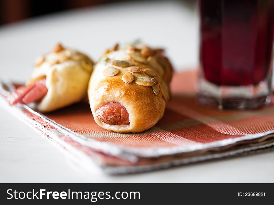 Two roll with sausage on the table and a glass of juice. Two roll with sausage on the table and a glass of juice