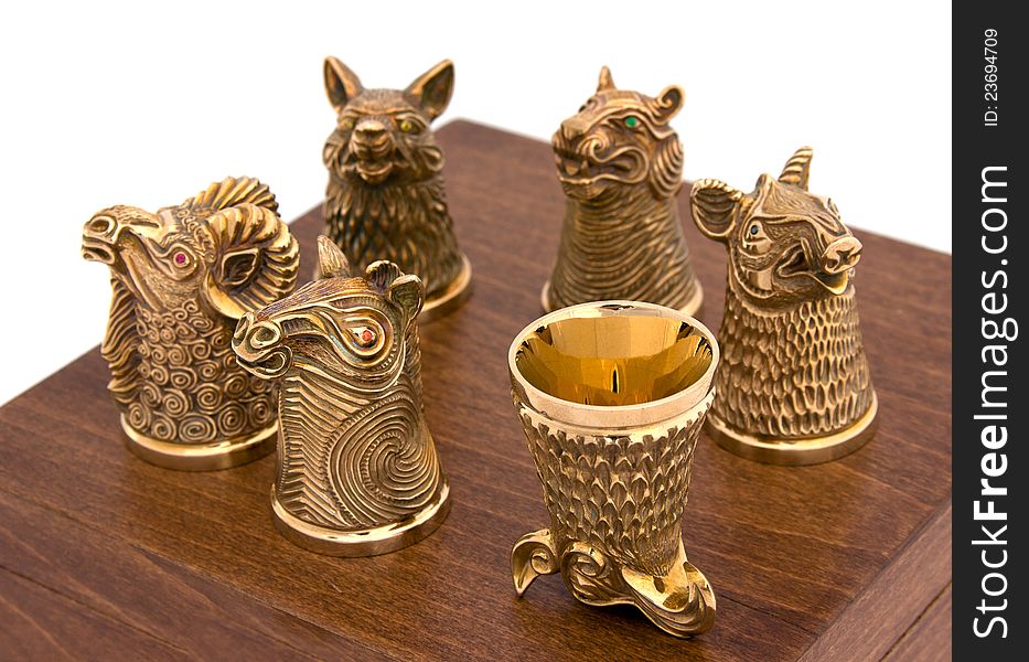 Golden animal-shaped glasses for strong spirits on the wooden box. Golden animal-shaped glasses for strong spirits on the wooden box