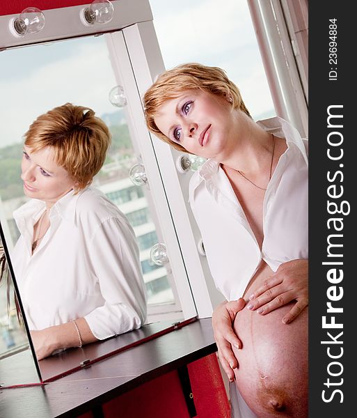 Beautiful pregnant woman daydreaming in front of a mirror