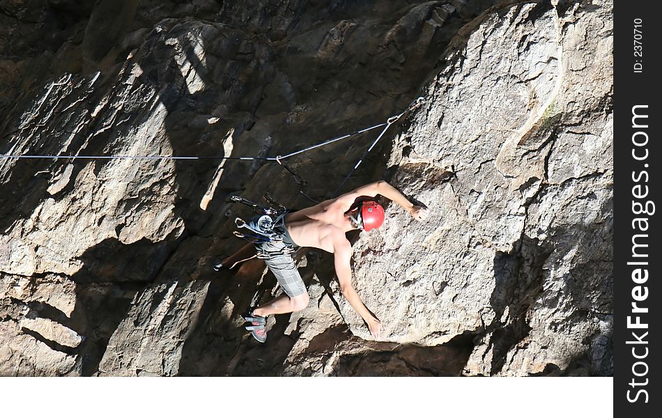 A rock climber works his way up a rock face protected by a rope clipped into bolts. He is wearing a helmet and quickdraws dangle from his harness. The route is in the desert southwest United States. Mt Lemmon, Arizona. A rock climber works his way up a rock face protected by a rope clipped into bolts. He is wearing a helmet and quickdraws dangle from his harness. The route is in the desert southwest United States. Mt Lemmon, Arizona.