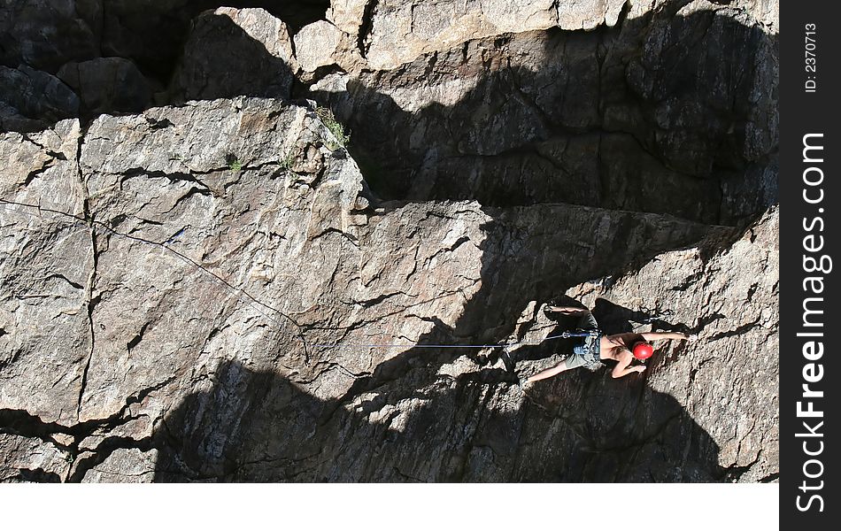 A rock climber works his way up a rock face protected by a rope clipped into bolts. He is wearing a helmet and quickdraws dangle from his harness. The route is in the desert southwest United States. Mt Lemmon, Arizona. A rock climber works his way up a rock face protected by a rope clipped into bolts. He is wearing a helmet and quickdraws dangle from his harness. The route is in the desert southwest United States. Mt Lemmon, Arizona.