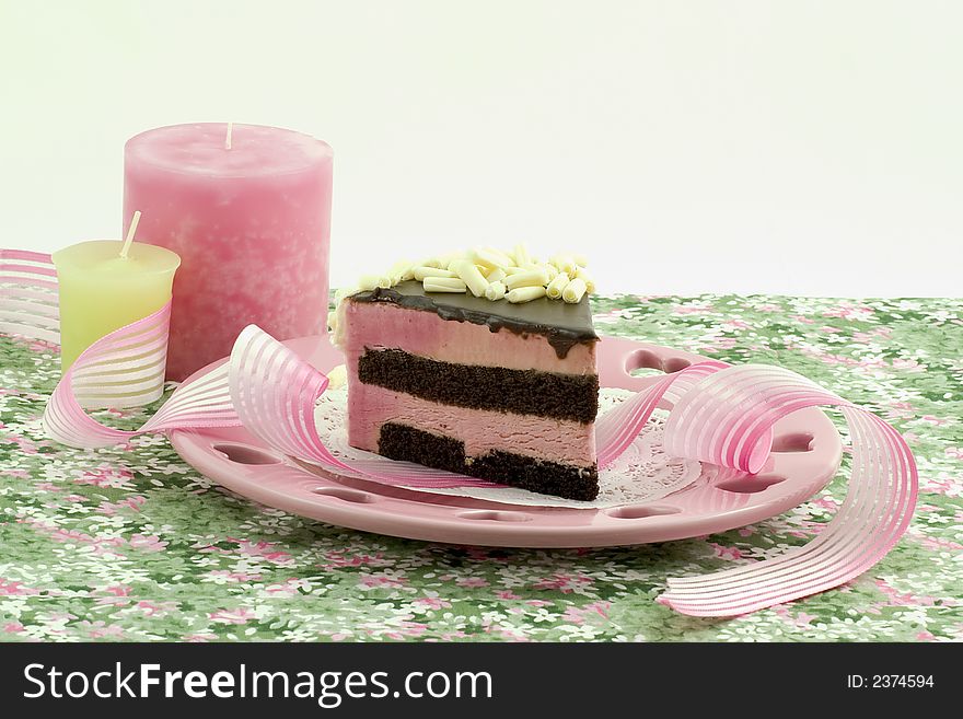 Raspberry mousse with chocolate cake decorated with white chocolate rolls, placed on a pink heart plate with delicate ribbon and lovely candles. Raspberry mousse with chocolate cake decorated with white chocolate rolls, placed on a pink heart plate with delicate ribbon and lovely candles.