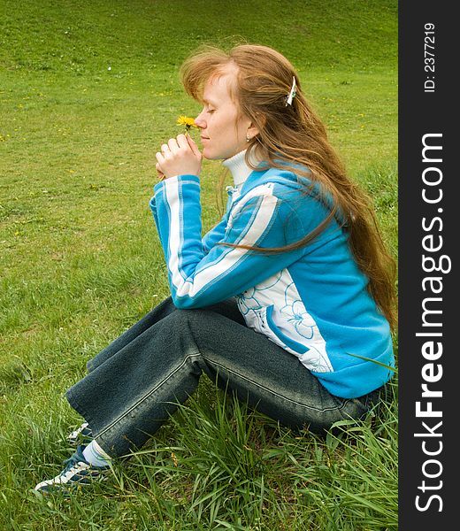 The red girl sits on a grass and holds a flower. The red girl sits on a grass and holds a flower