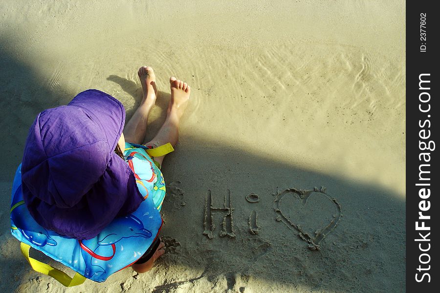 Young child sitting on the sand at the beach - love message in the sand. Young child sitting on the sand at the beach - love message in the sand