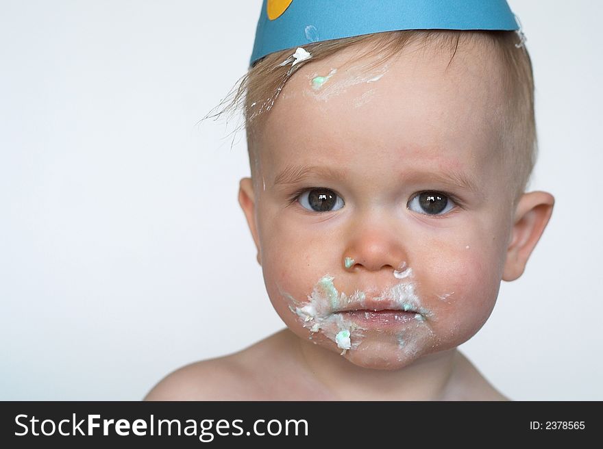 Image of an adorable 1 year old, wearing a paper hat, with cake frosting all over his face. Image of an adorable 1 year old, wearing a paper hat, with cake frosting all over his face