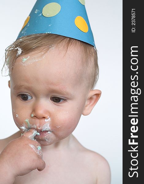 Image of an adorable 1 year old, wearing a paper hat, eating birthday cake. Image of an adorable 1 year old, wearing a paper hat, eating birthday cake