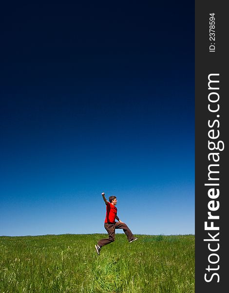 Active happy young man jumping in a green field against a clear blue sky. Active happy young man jumping in a green field against a clear blue sky