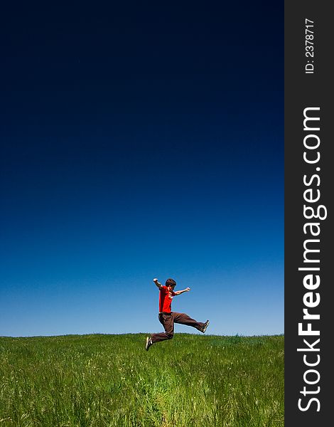 Active happy young man jumping in a green field against a clear blue sky. Active happy young man jumping in a green field against a clear blue sky