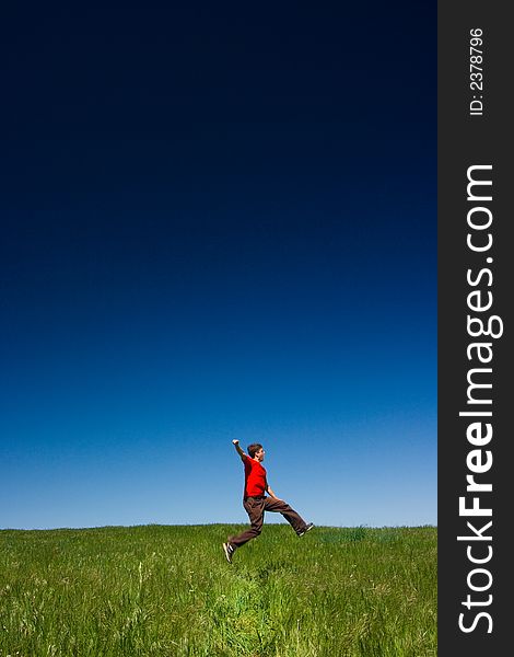 Active happy young man jumping in a green field against a clear blue sky. Active happy young man jumping in a green field against a clear blue sky